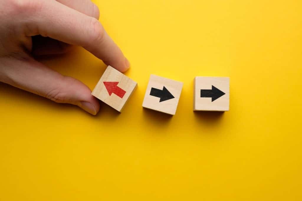 In the picture you can see three wooden cubes on a yellow background. There is an arrow on each cube. The first dice, held by the hand, has a red arrow pointing to the left. The second and third dice have black arrows pointing to the right.