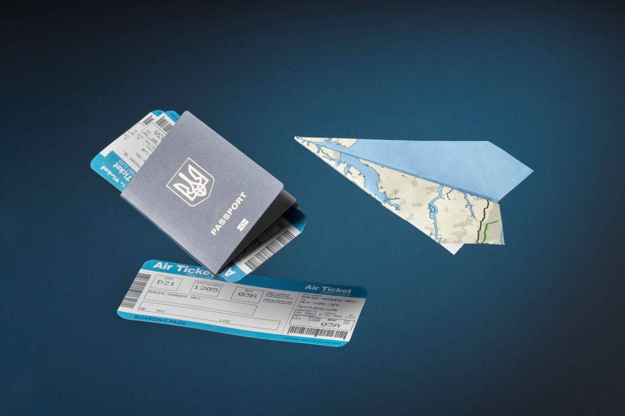 Obraz przedstawia paszport, dwa bilety lotnicze i papierową samolotikę. Paszport jest niebieski z białym emblematem na okładce, a bilety lotnicze są oznaczone jako "Air Ticket" i "Boarding Pass." Papierowa samolotika jest wykonana z mapy.